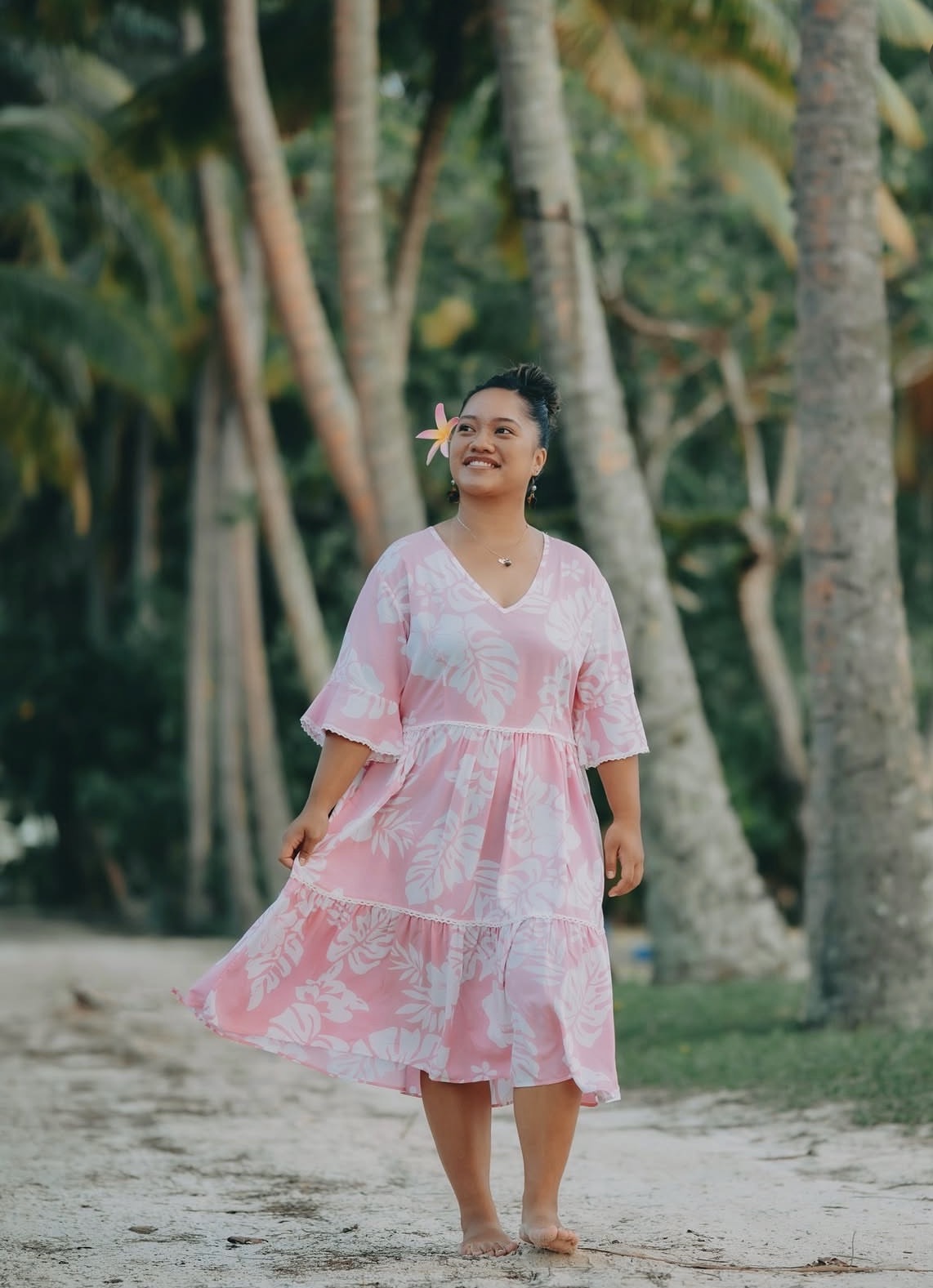 Three women in colourful floral dresses and woven hats looking out at the Rarotonga mountains